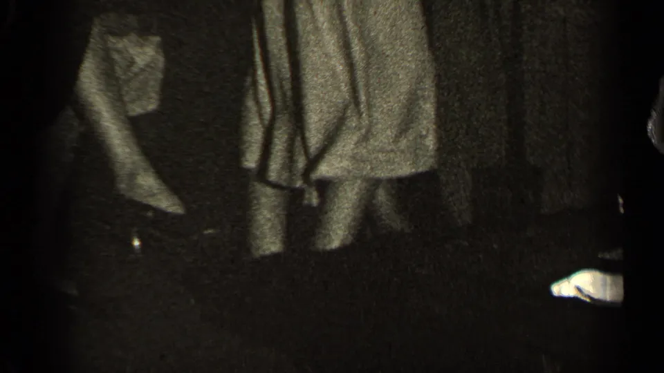 A dark 1947 Illinois interior shows partially visible people standing near coats or garments, with faces mostly obscured by exposure and framing.