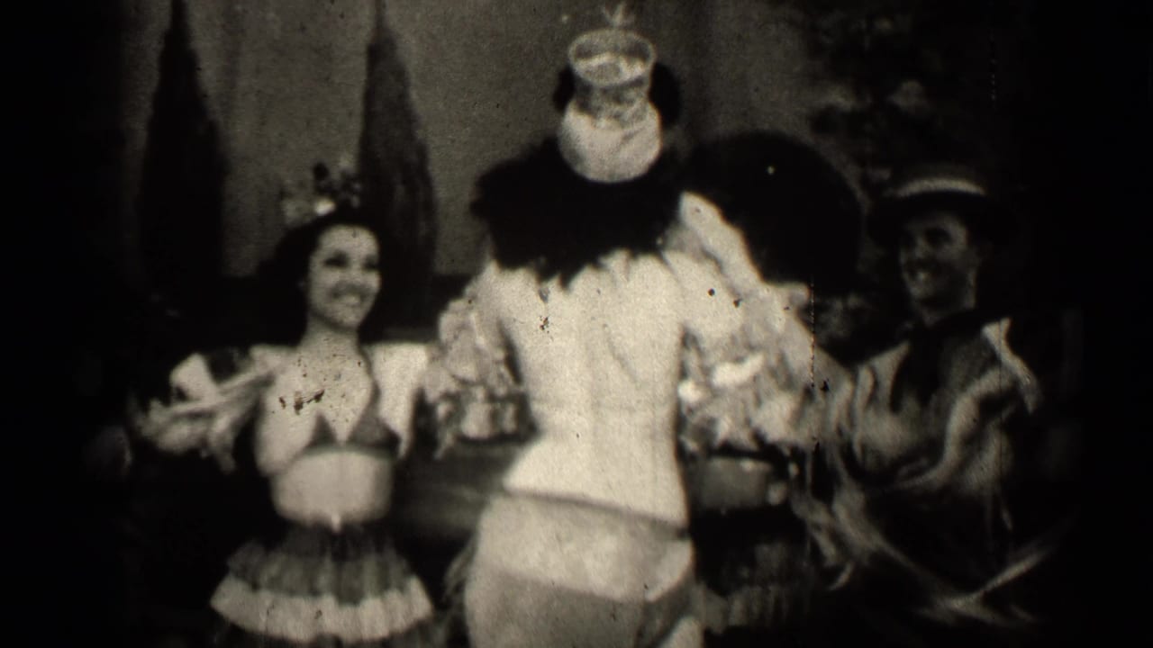Costumed woman in a grass skirt faces a clown-costumed performer while another performer stands nearby.