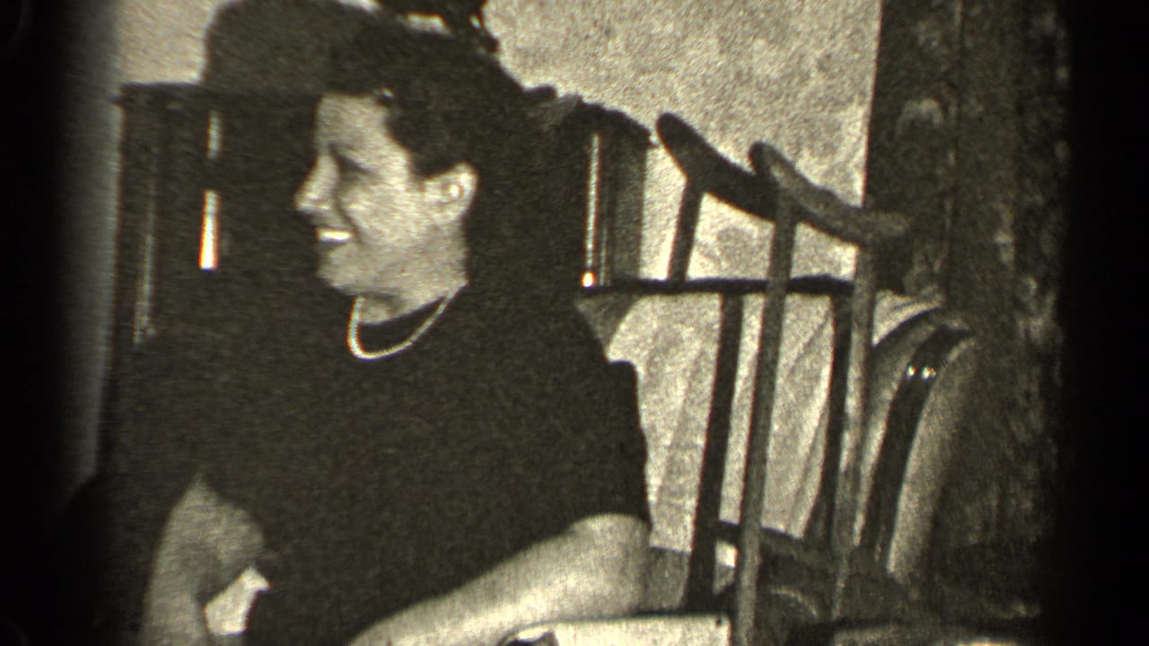 In a 1947 Illinois home-movie frame, a woman in a dark dress and pearl necklace smiles as a small bird sits on her head.