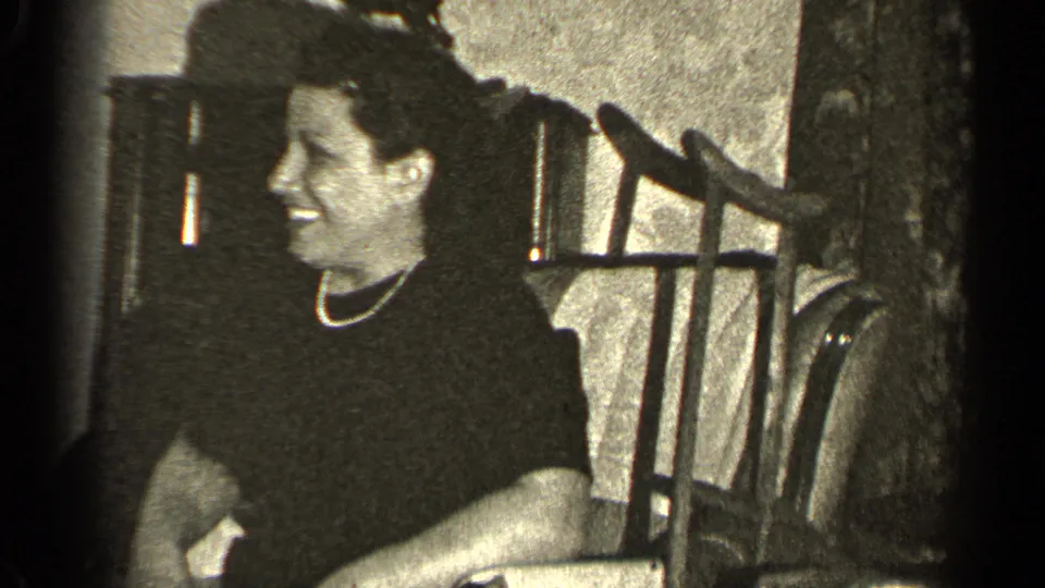 In a 1947 Illinois home-movie frame, a woman in a dark dress and pearl necklace smiles as a small bird sits on her head.