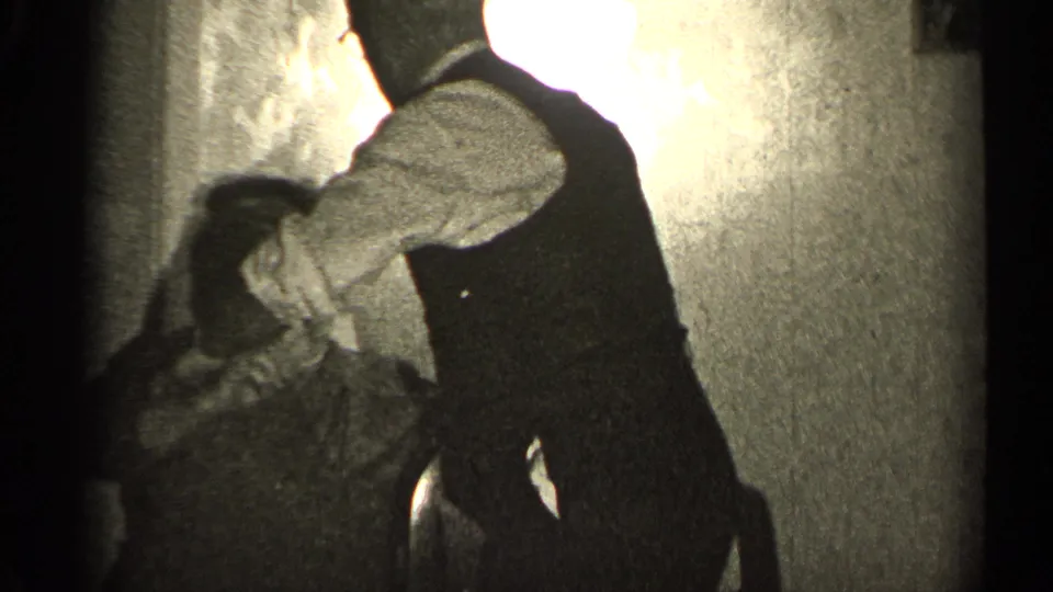 In a 1947 Illinois home-movie frame, a man in a dark vest appears to lean toward a seated woman in a shadowed room.