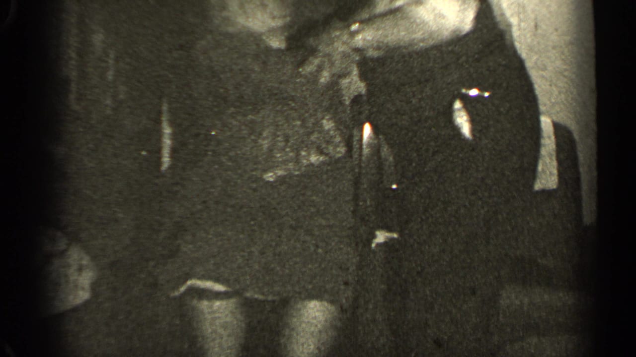 Dark, grainy view of the two adults near a chair and wall.