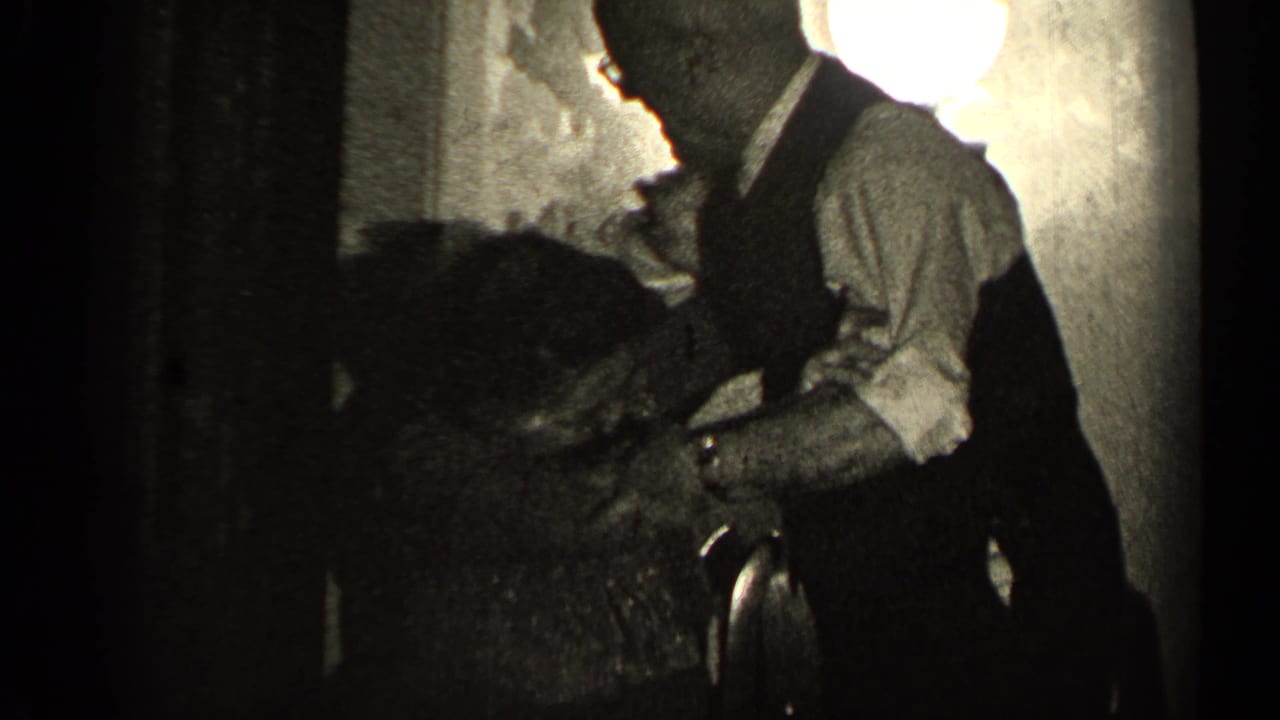 In 1947 Illinois home-movie footage, an older man in a vest bends toward an older woman in a low-lit private room.
