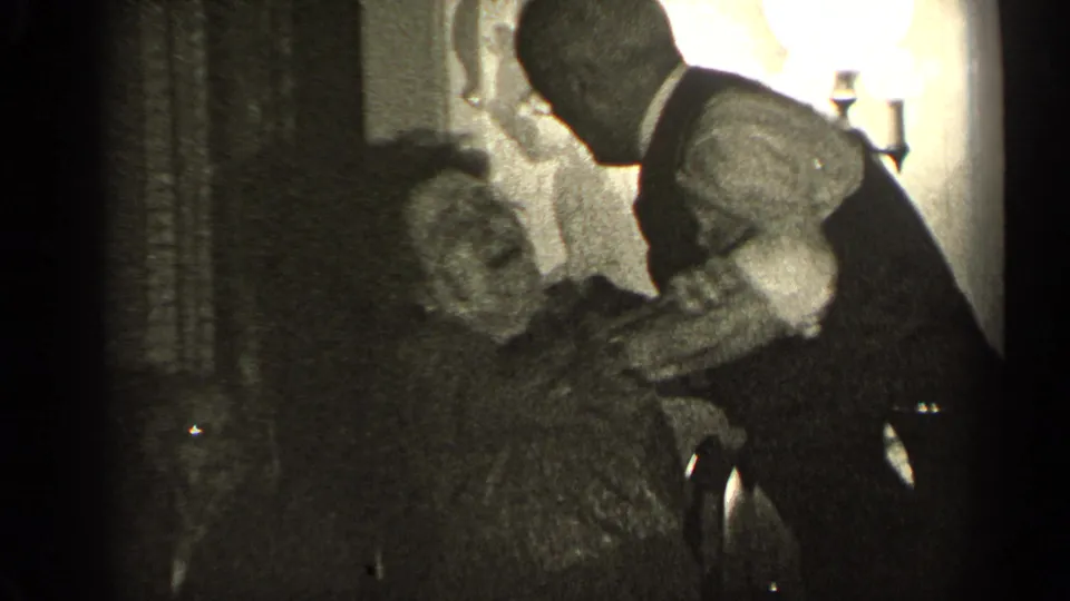 An older man bends close to an older woman who appears to laugh during a playful 1947 Illinois home-movie moment.