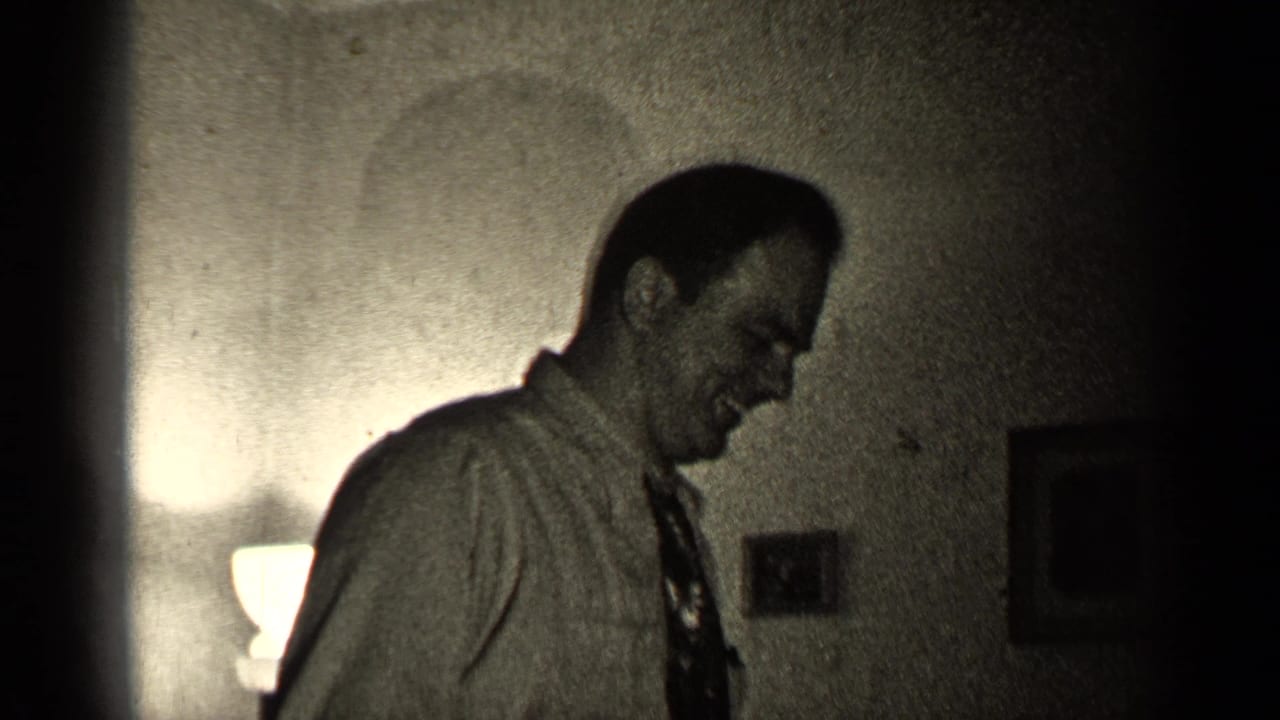 Man in a collared shirt and tie smiles in a dimly lit room.