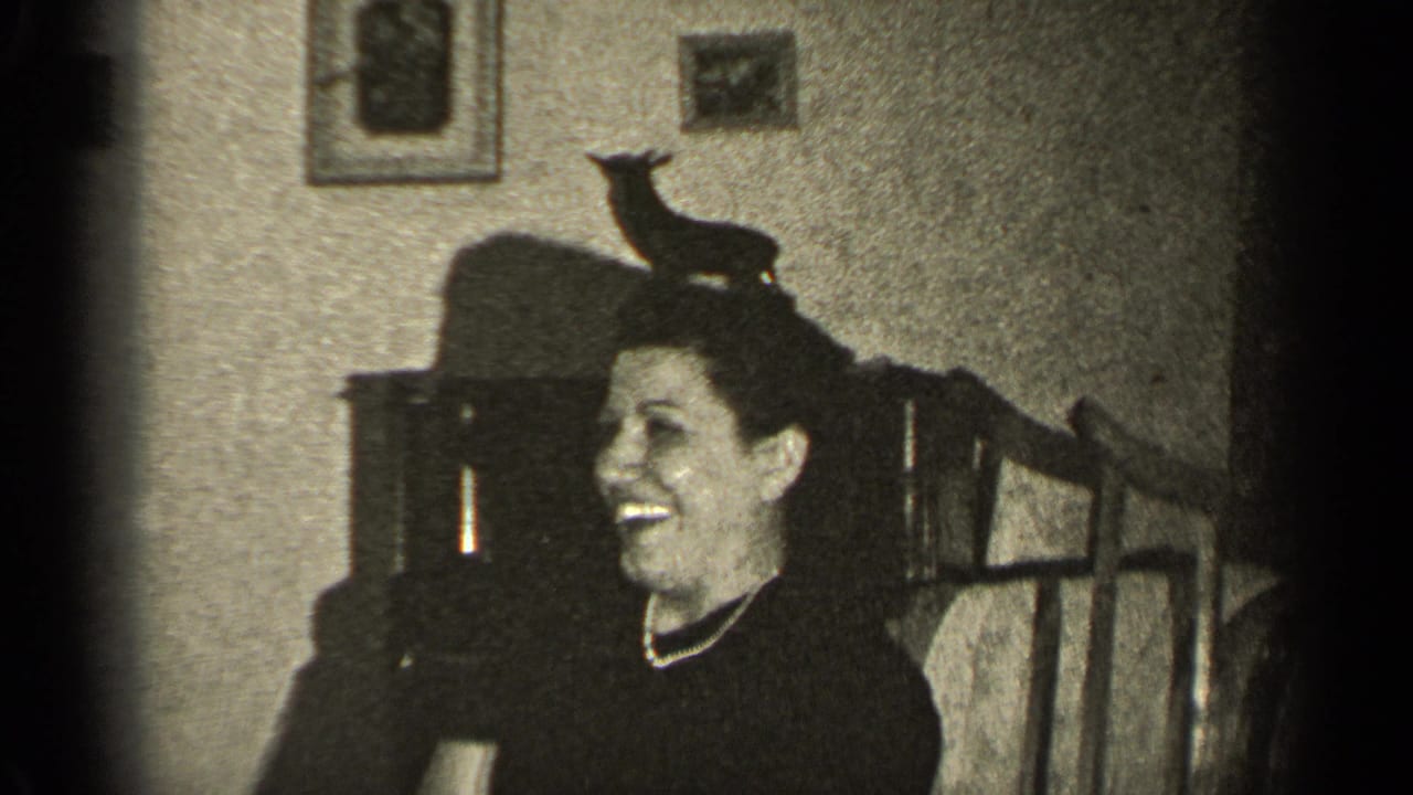 A smiling woman sits in a 1947 Illinois interior, with framed pictures, dark furniture, and a small animal-shaped object nearby.