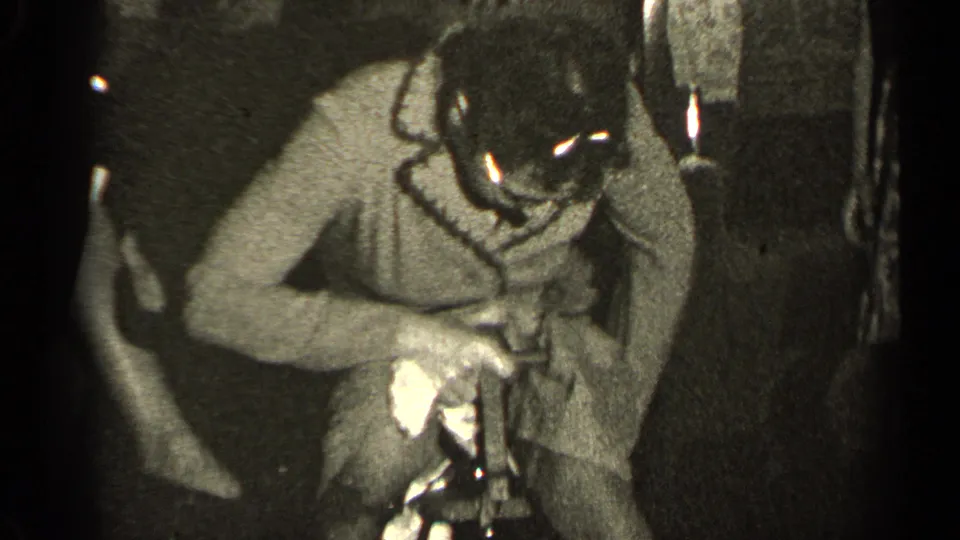 In the 1947 Illinois home-movie footage, a person bends over a small project while another figure stands partly visible nearby.