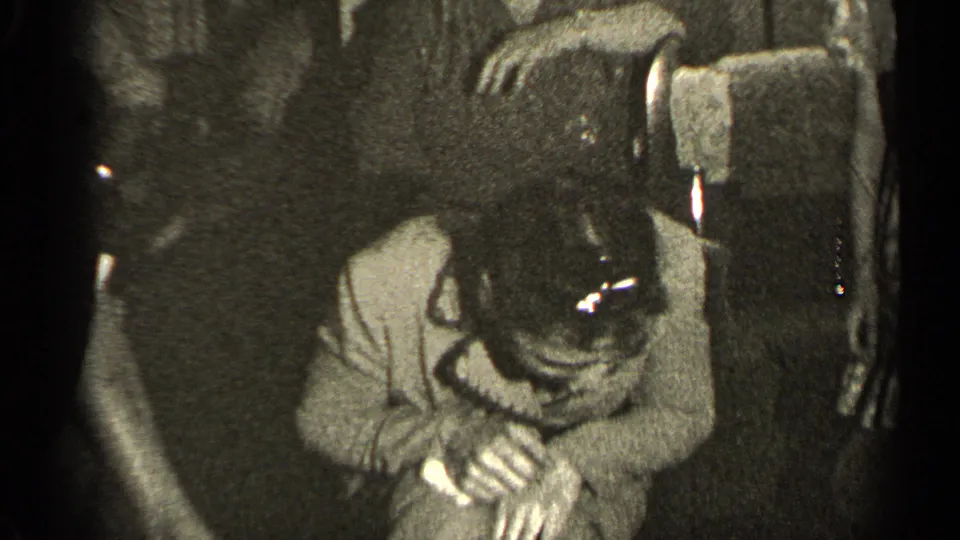 A 1947 Illinois home-movie frame shows a person leaning over a small object near upholstered furniture in a private interior.