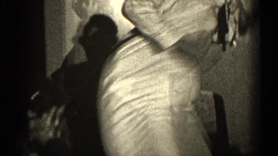 In 1947 Illinois home-movie footage, a woman in dressy clothing dances in a dim private interior with another figure partly visible.