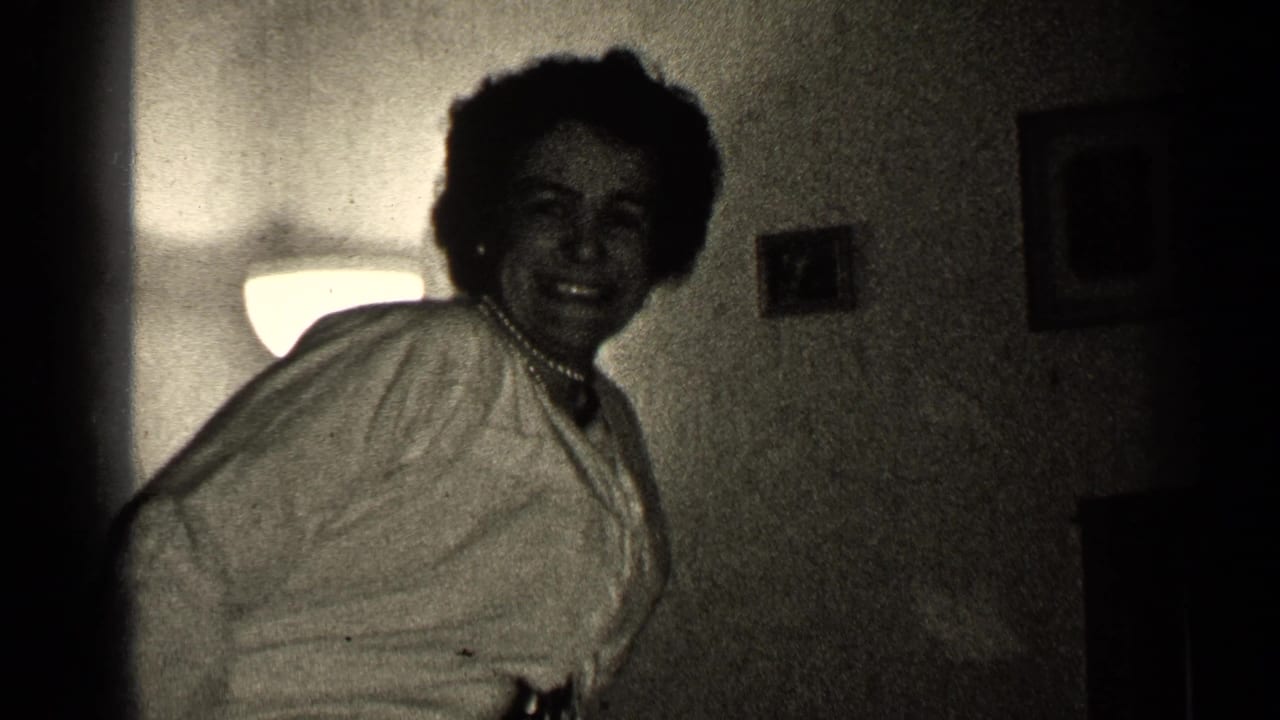 Smiling woman in a light blouse dances near a glowing wall lamp.