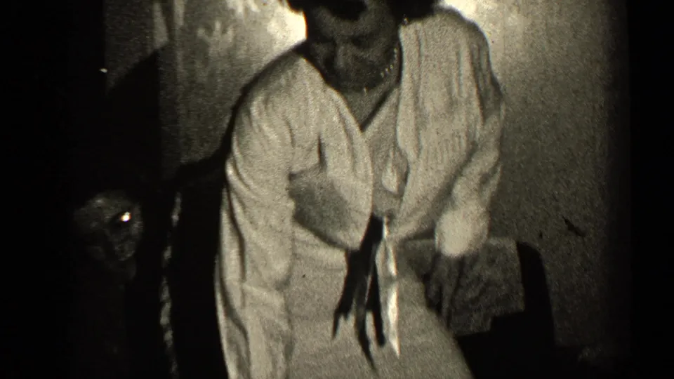 A woman in a light blouse leans forward mid-dance in a 1947 Illinois home interior, with another adult partly visible behind her.