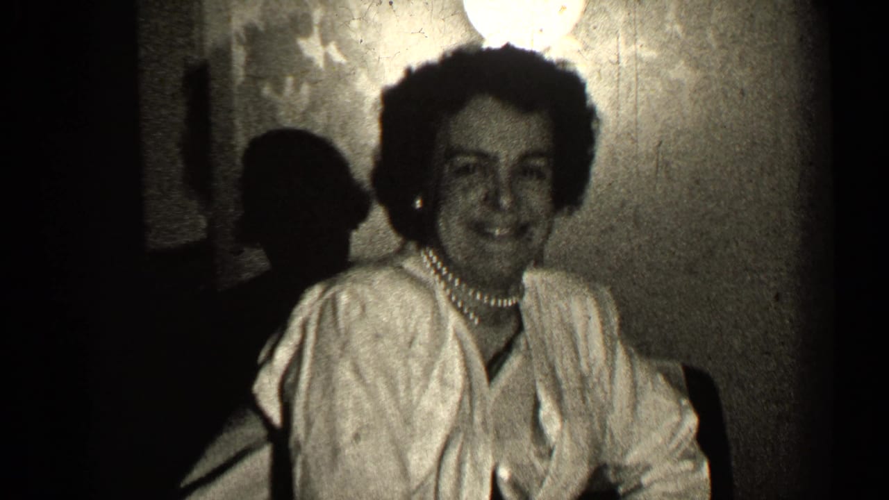 Woman smiles toward the camera while seated in a dim interior.