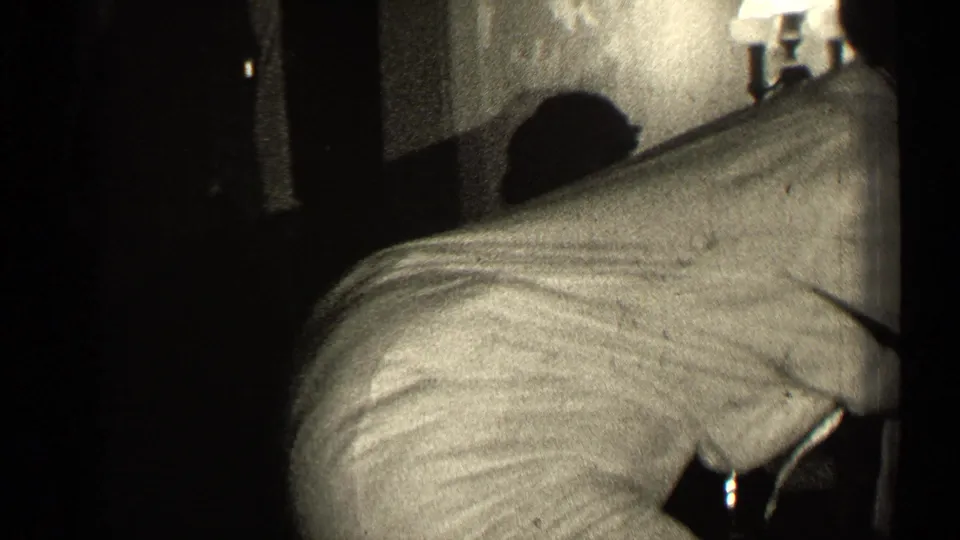 The woman bends or leans in the 1947 Illinois home-movie scene, with the pillow shape visible beneath or against her light dress.