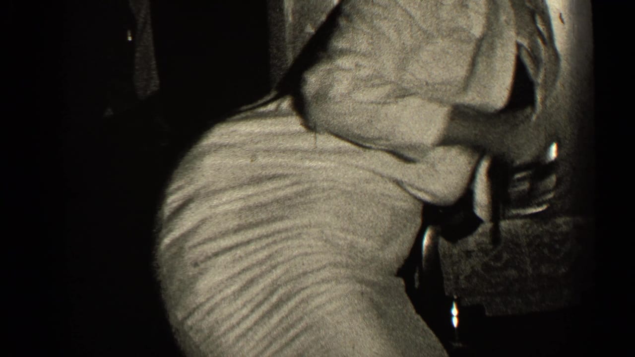 Close view of a seated person leaning over a wrapped gift in a dark interior.