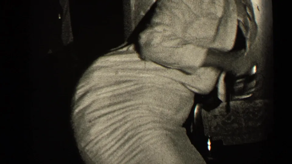 1947 Illinois 8mm frame showing a seated adult leaning forward over a wrapped Christmas gift in a dim private interior.
