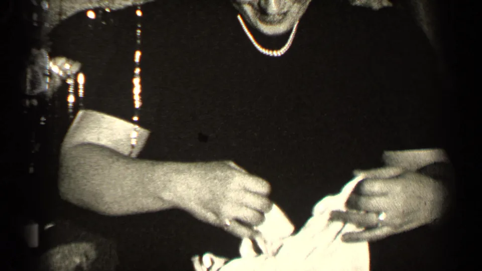 1947 Illinois 8mm frame showing hands opening a pale wrapped Christmas package against a dark dress and dim room.