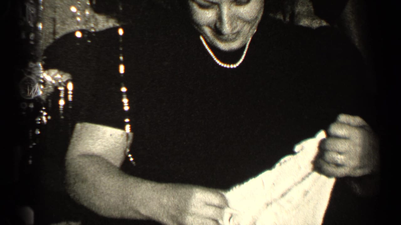 Woman in a dark dress holds light-colored fabric in a dim room.