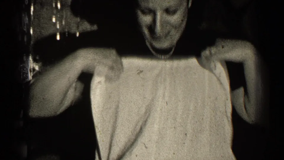 The woman holds the light-colored garment open across her chest while smiling in the 1947 Illinois home-movie frame.