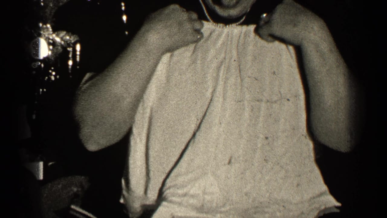 Woman in a light sleeveless top holds something near her face in a dark room.