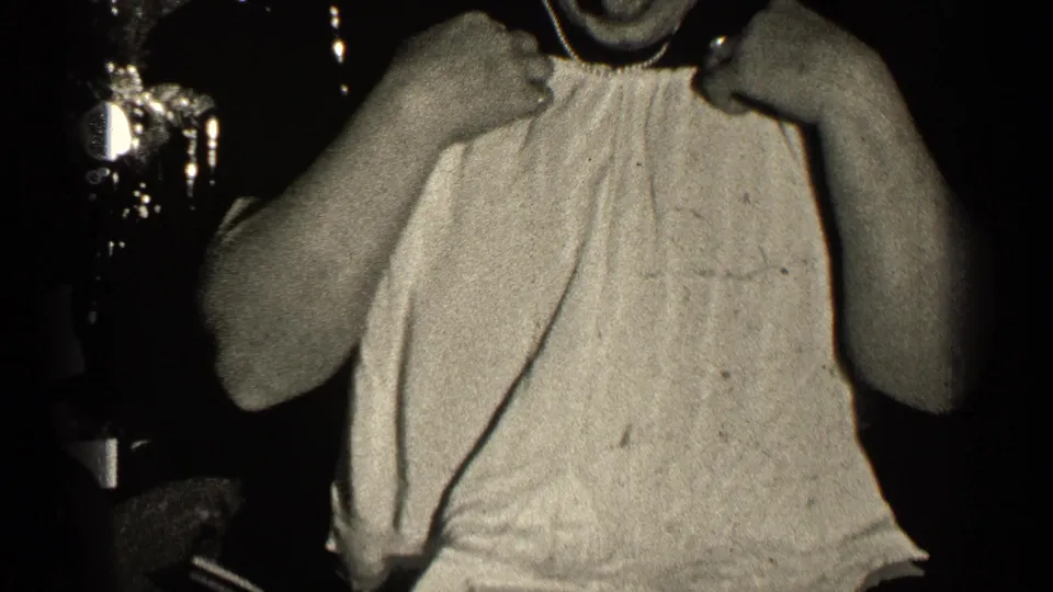 In 1947 Illinois home-movie footage, a woman in a light sleeveless garment is closely framed in a dim private interior.