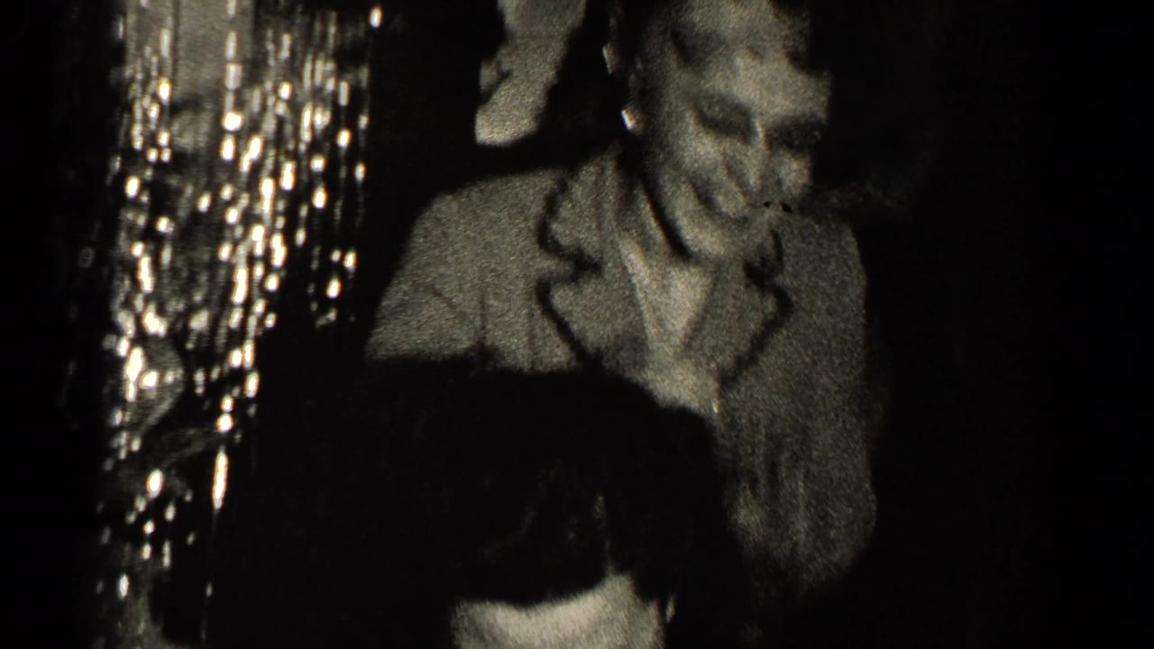 Older woman smiles beside another figure in a dark, chandelier-lit room.