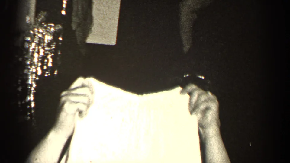 A woman in a dark dress and necklace holds up a light textured garment, possibly a baby outfit, during the 1947 Illinois gathering.