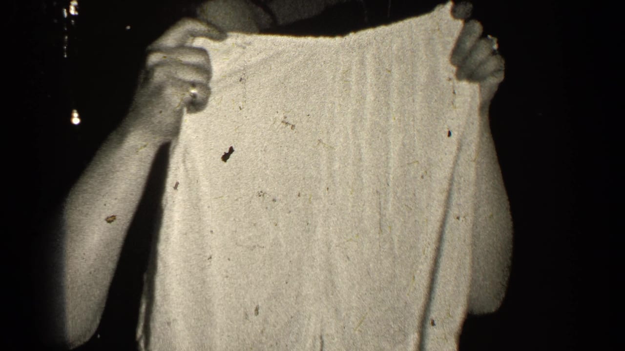 Hands hold up light-colored shorts against a dark background.