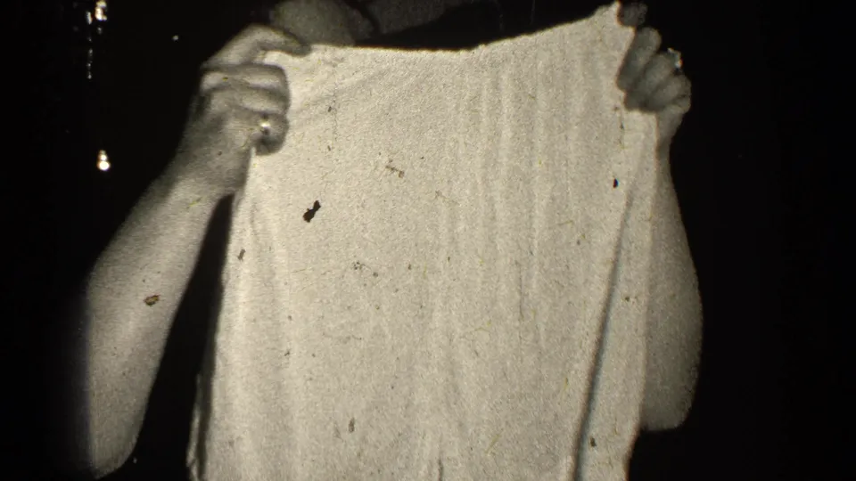 In 1947 Illinois home-movie footage, a woman partly out of frame holds up light-colored shorts in strong contrast against darkness.