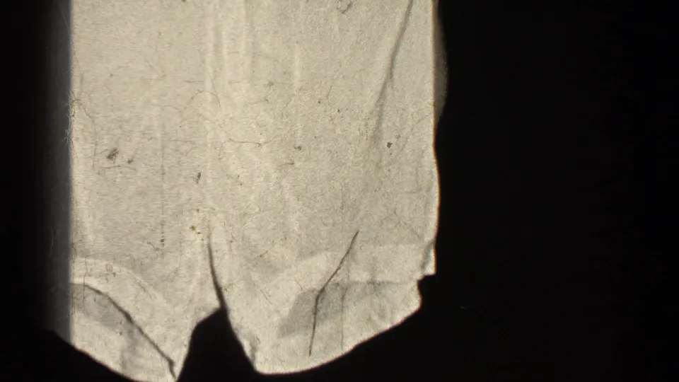 The shorts dominate the frame while the woman’s hands hold the waistband near the top in grainy 8mm footage.