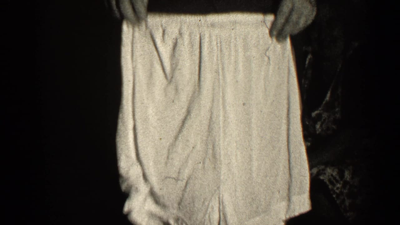 Hands hold up a light-colored garment against a dark background.