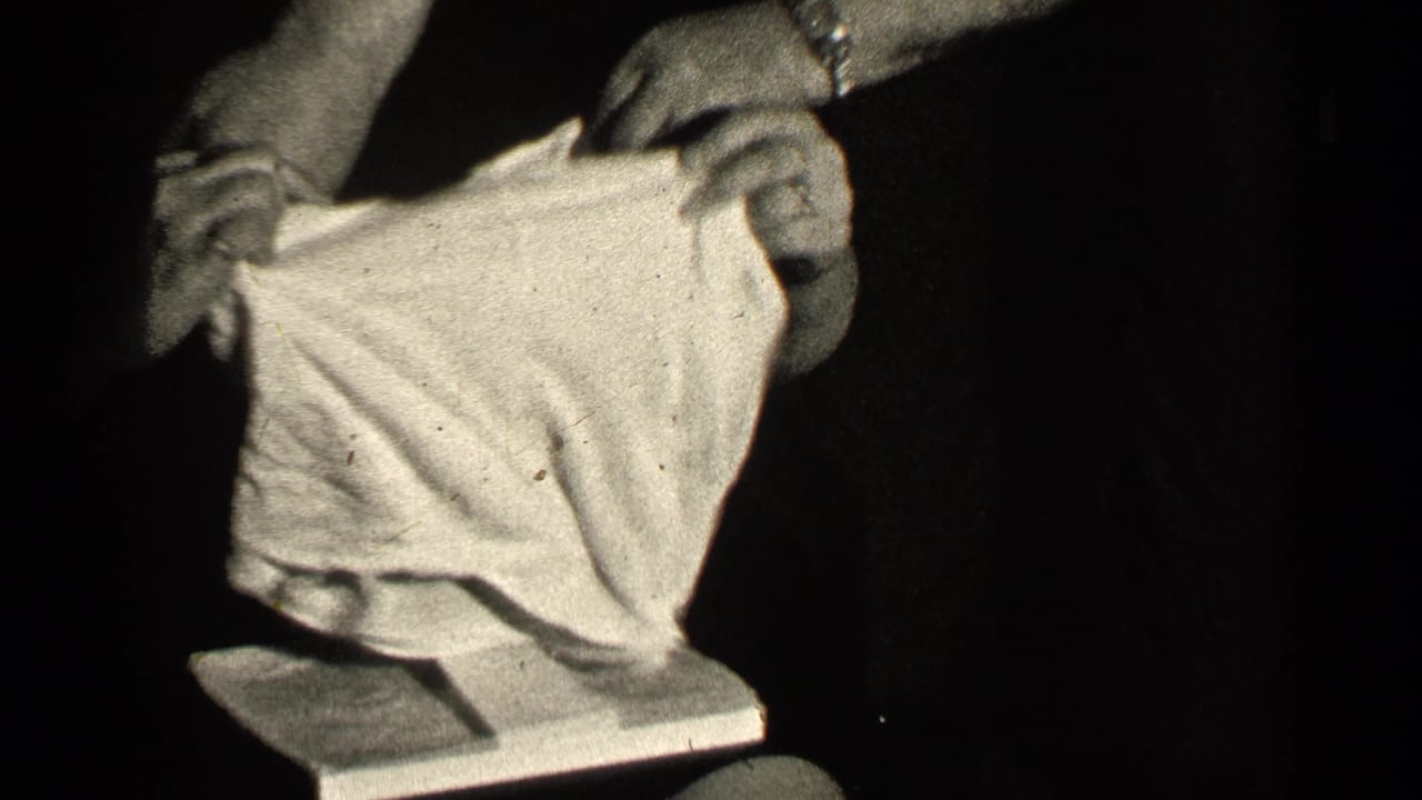 Hands hold up a light-colored garment against a dark background.