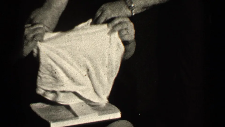 In 1947 Illinois home-movie footage, adult hands hold a light textured garment close to the camera in dim light.