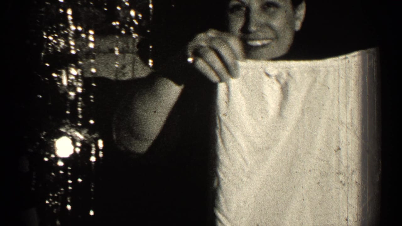 Smiling woman in a dark dress holds up a light-colored garment or cloth indoors.