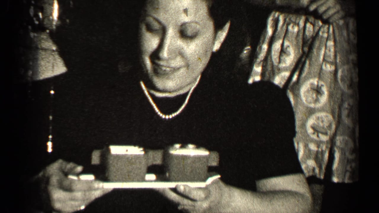 Woman in dark dress and pearls holds a small tray in a dim indoor gathering.