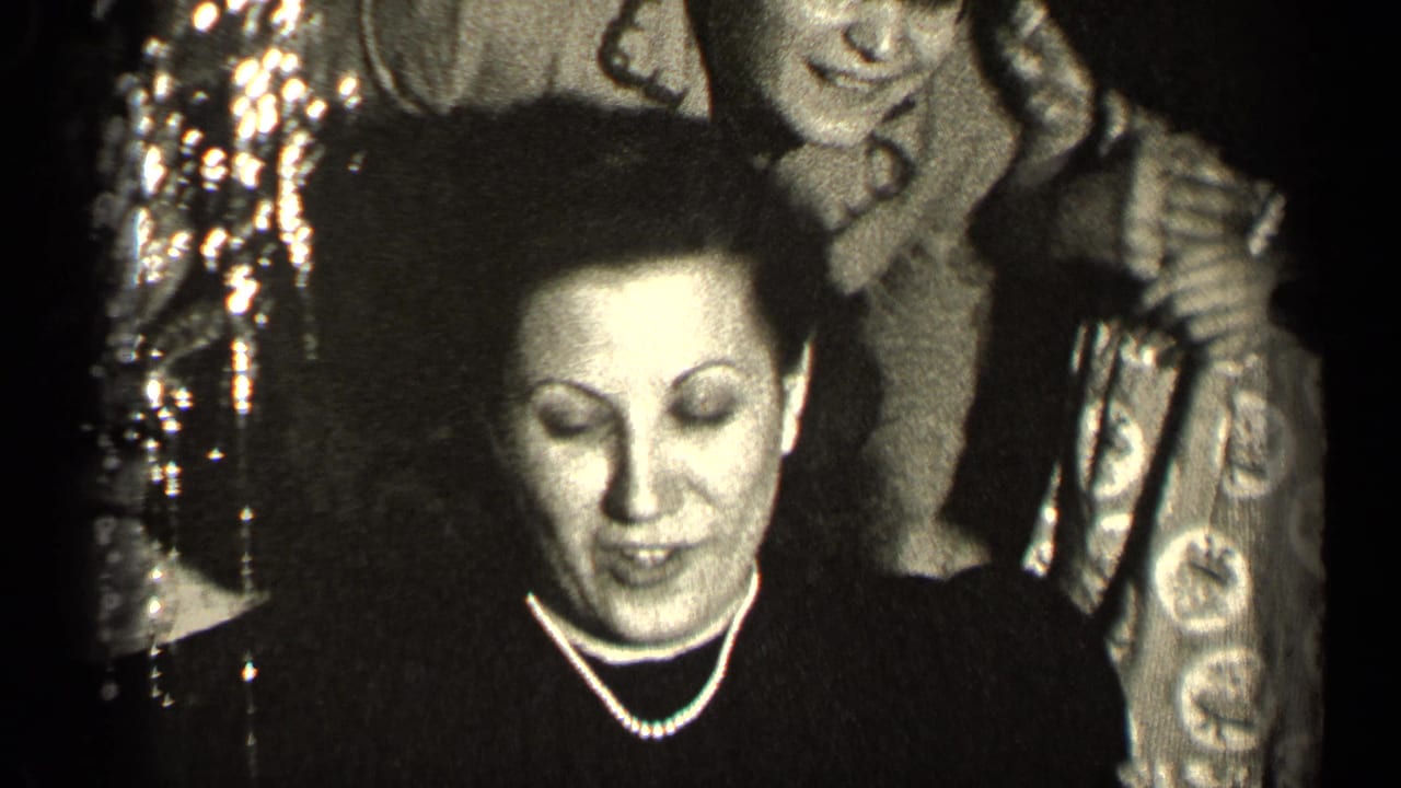 Woman in dark dress looks down while smiling, with others standing behind her.