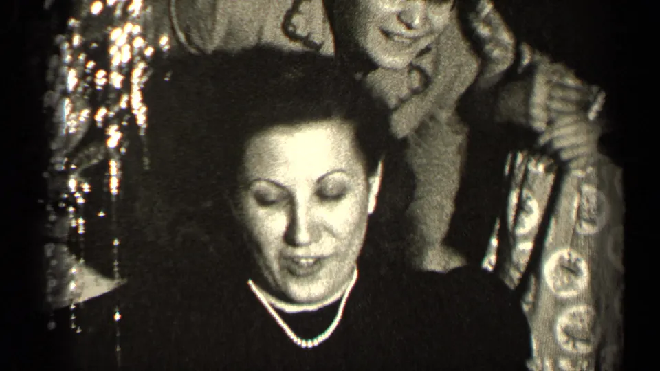 The woman in pearls looks down with a small smile as nearby figures crowd into the dim private interior.