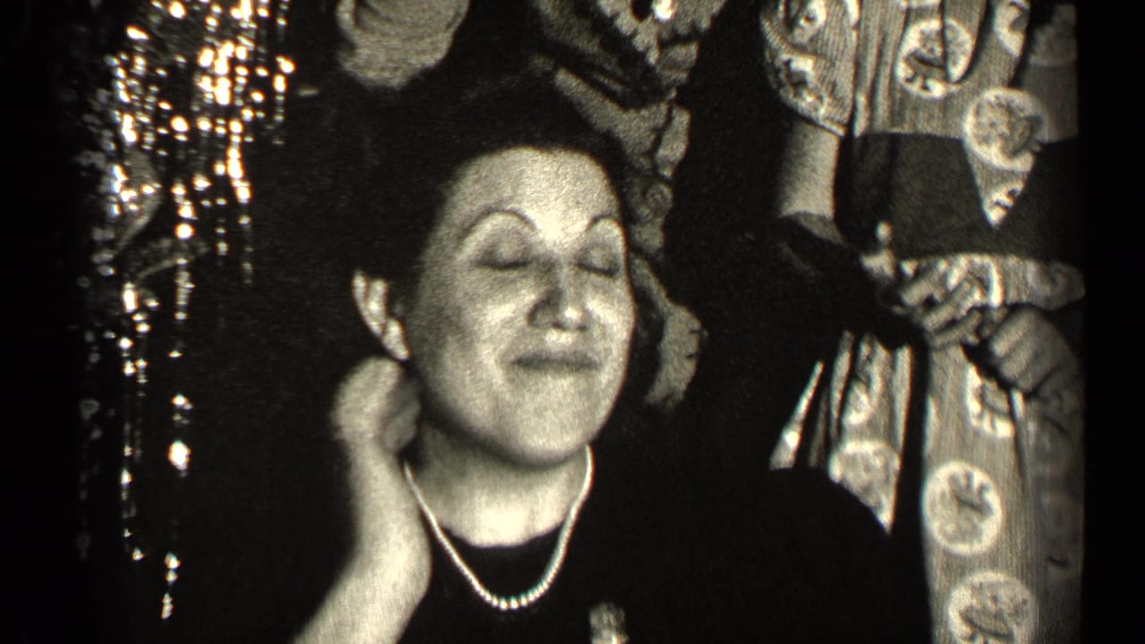The woman closes her eyes and touches her neck, appearing to enjoy the scent during the 1947 Illinois indoor gathering.