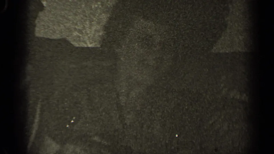 Grainy 1947 Illinois 8mm frame of two adults seated close together on a couch, their faces partly obscured by shadow.