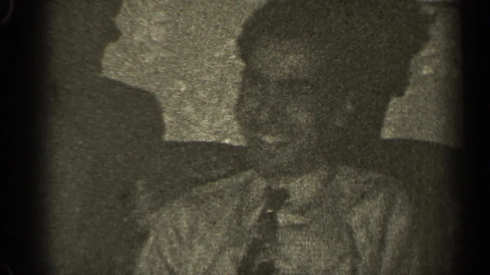 The final 1947 Illinois 8mm frame shows the couch scene continuing, with the man and woman largely in silhouette and soft grain.