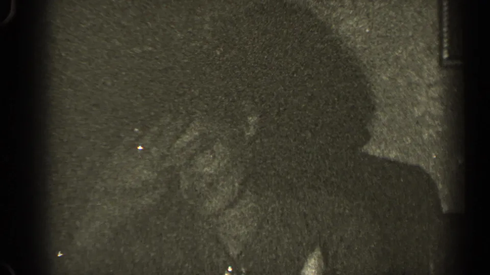 Grainy 1947 Illinois home-movie frame with adults seated indoors, one figure turned in profile during conversation.