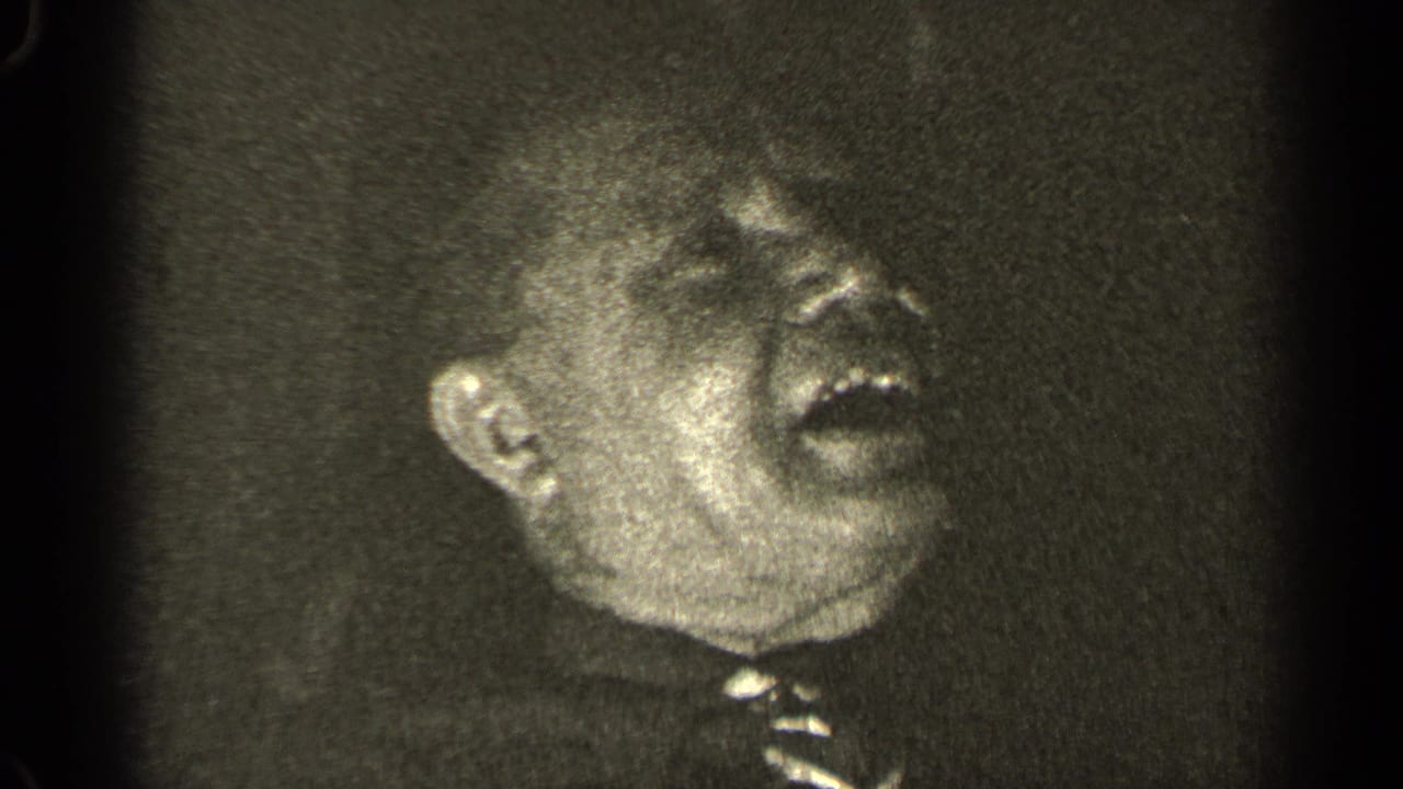 Older man turns slightly while laughing in soft-focus 8mm footage.