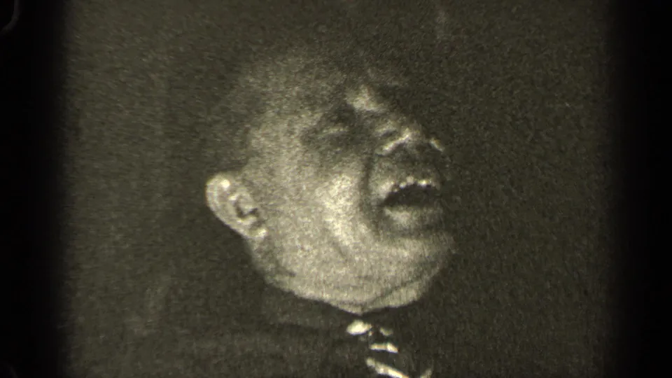 Older man in 1947 Illinois footage laughs with his head angled to the side, tie and collar partly visible.