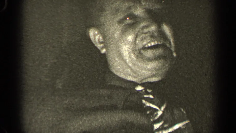 Older man in shirt and tie continues laughing in close-up, shown in black-and-white 1947 Illinois 8mm footage.