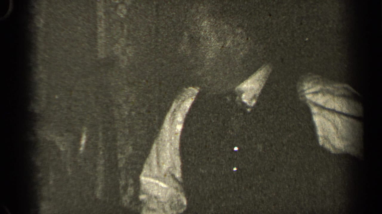 Adult torso in a dark vest with light sleeves against a dim background.