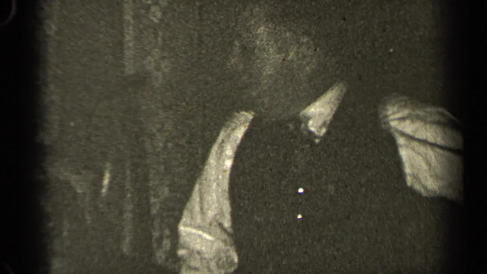 1947 Illinois 8mm frame with a partial adult figure in a dark vest and light shirt, cropped by the edge of the shot.