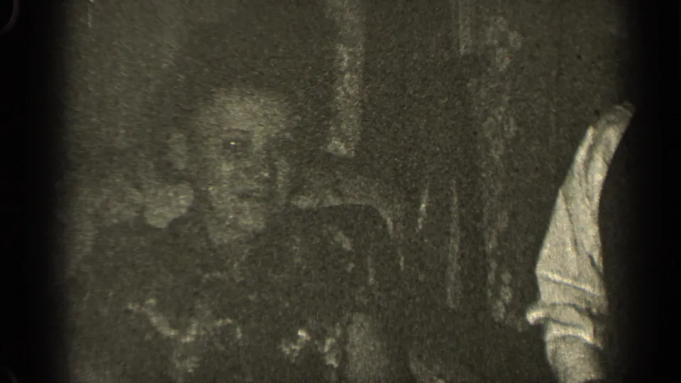 Low-exposure 1947 Illinois frame showing partial adults, a light sleeve, and a dark textured background.