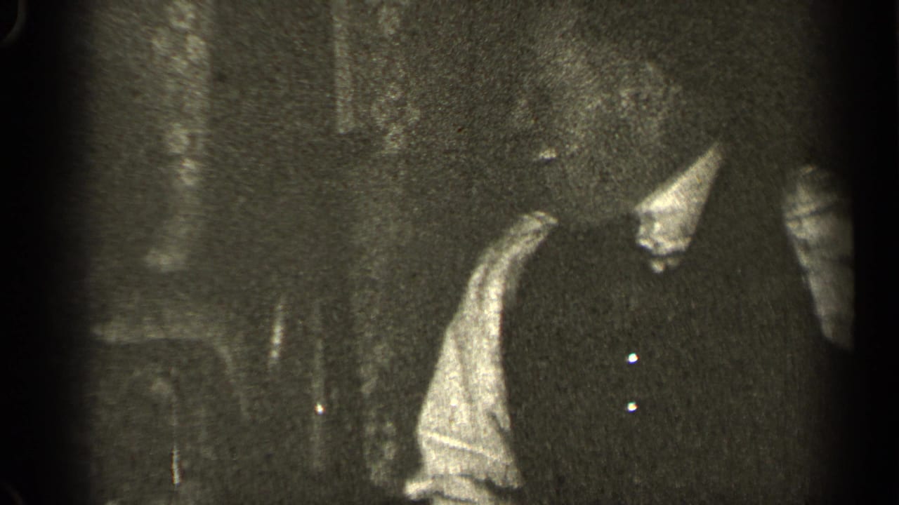 Adult in dark vest or dress standing in a dim indoor room.