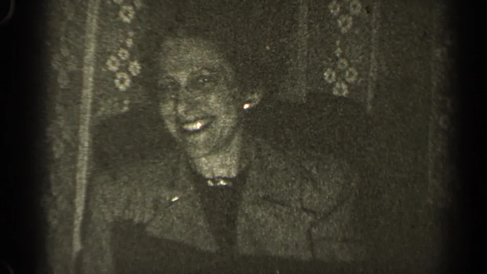 A woman smiles broadly at an indoor Illinois gathering in grainy 1947 black-and-white 8mm footage.