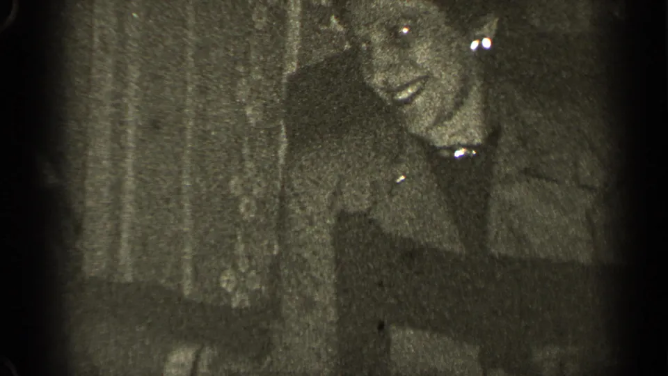 1947 8mm home-movie frame from Illinois showing an older person partly obscured by darkness, grain, and film wear.