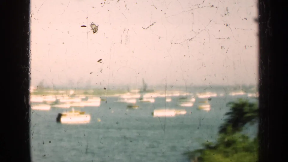 1947 Illinois 8mm frame showing boats on a harbor or lake through dark window bars, with foliage in the foreground.
